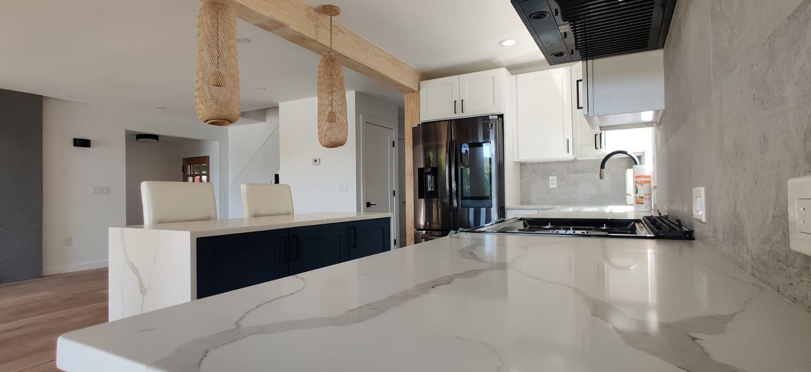Waterfall quartz island with navy cabinetry and woven pendants